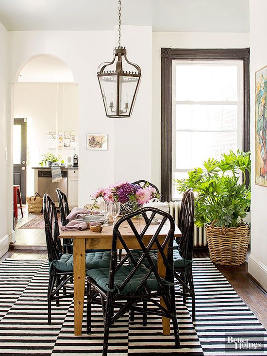 BHG-Design aspects such as the striped rug and sleek black Chippendale chairs play off a humble wood farm table in the room.